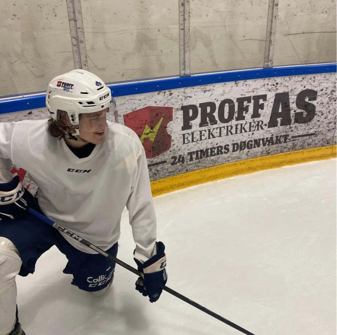 Ishockeyspiller foran en vant med reklame for Proff Elektriker